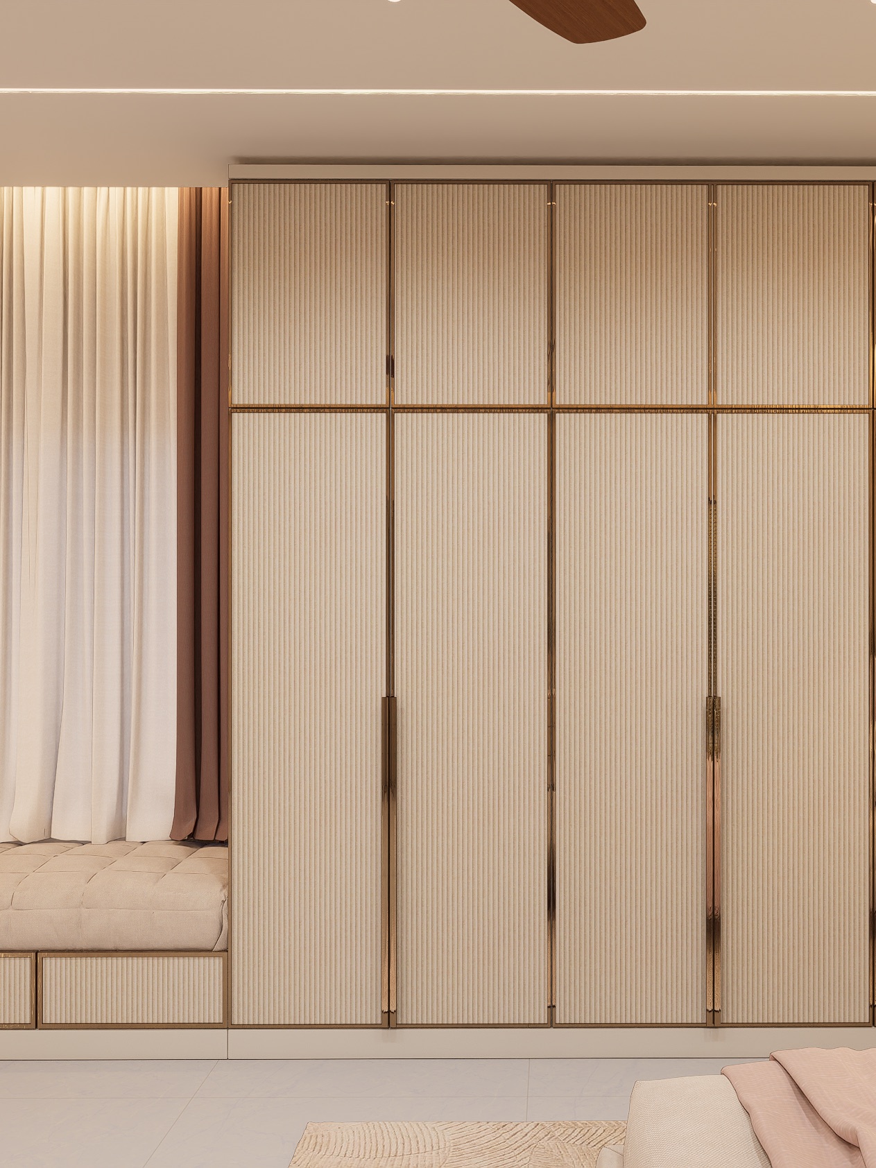 A full-height wardrobe of four tall beige fluted hinged shutters with slim metallic edge trims and long pull handles, a row of matching loft shutters above, and an upholstered window seat with fluted drawers beside it.