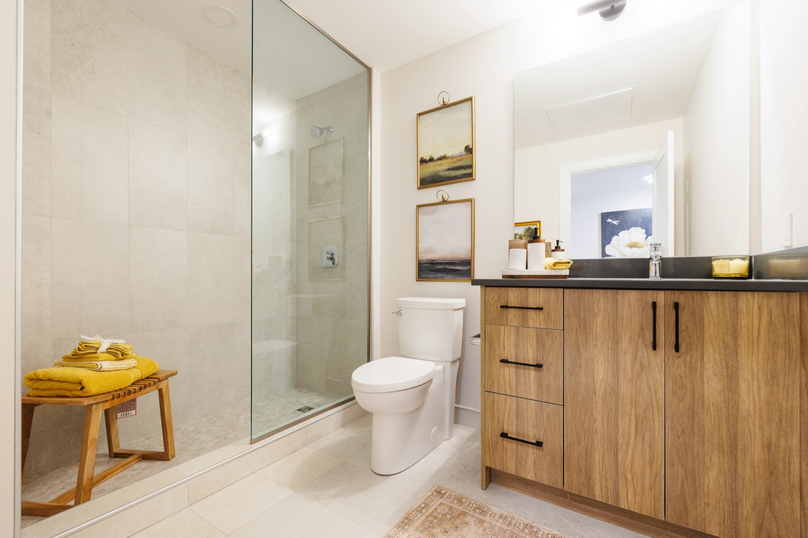Bathroom with a frameless glass walk-in shower, a wall-mounted shower head and a single concealed mixer plate on large beige tiles, beside a WC and a wood-finish vanity with a chrome basin mixer
