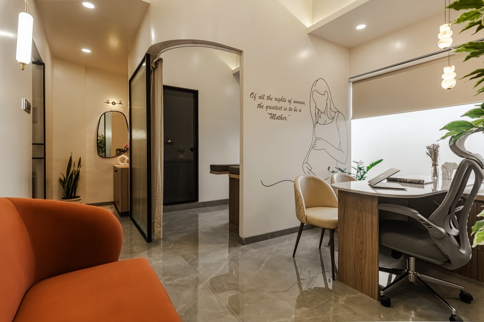 Interior of a small clinic with a curved orange sofa in the foreground, a timber and white consultation desk with grey chairs by a window, an arched opening to an examination area and a line drawing of a pregnant woman on the wall