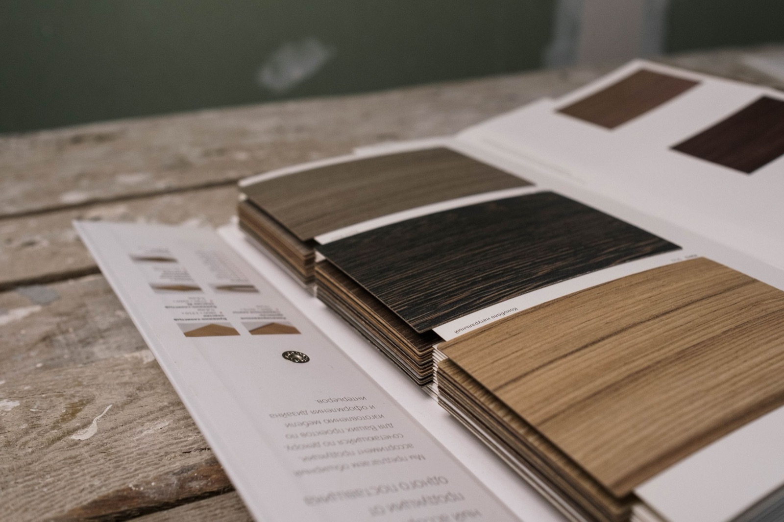 An open shade book of thin wood-grain finish samples on a workbench, fanned out in grey oak, near-black and warm natural oak tones