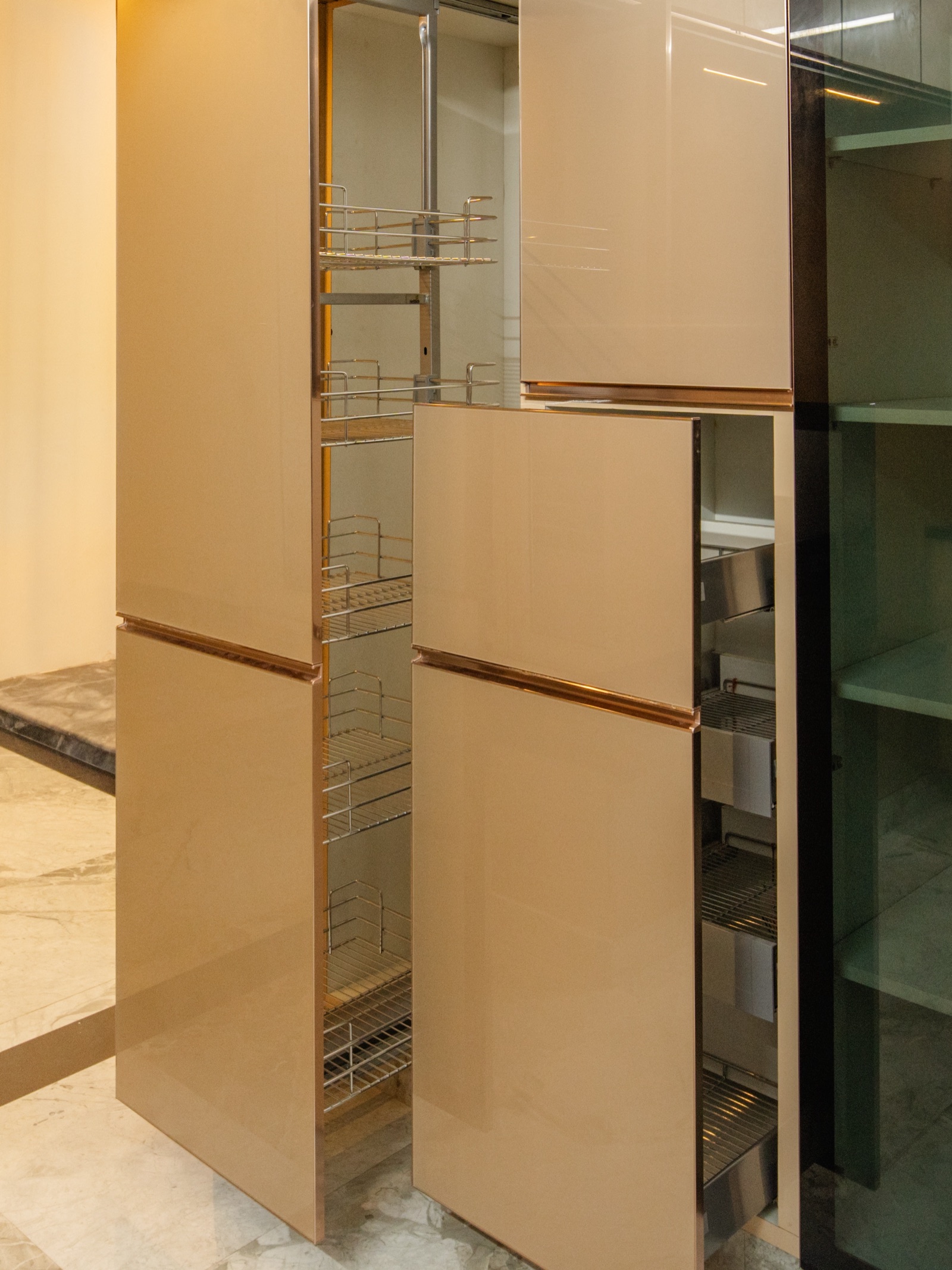 Tall kitchen pantry units with glossy champagne-coloured shutters pulled open to show multi-tier wire pull-out baskets and stacked steel drawers inside