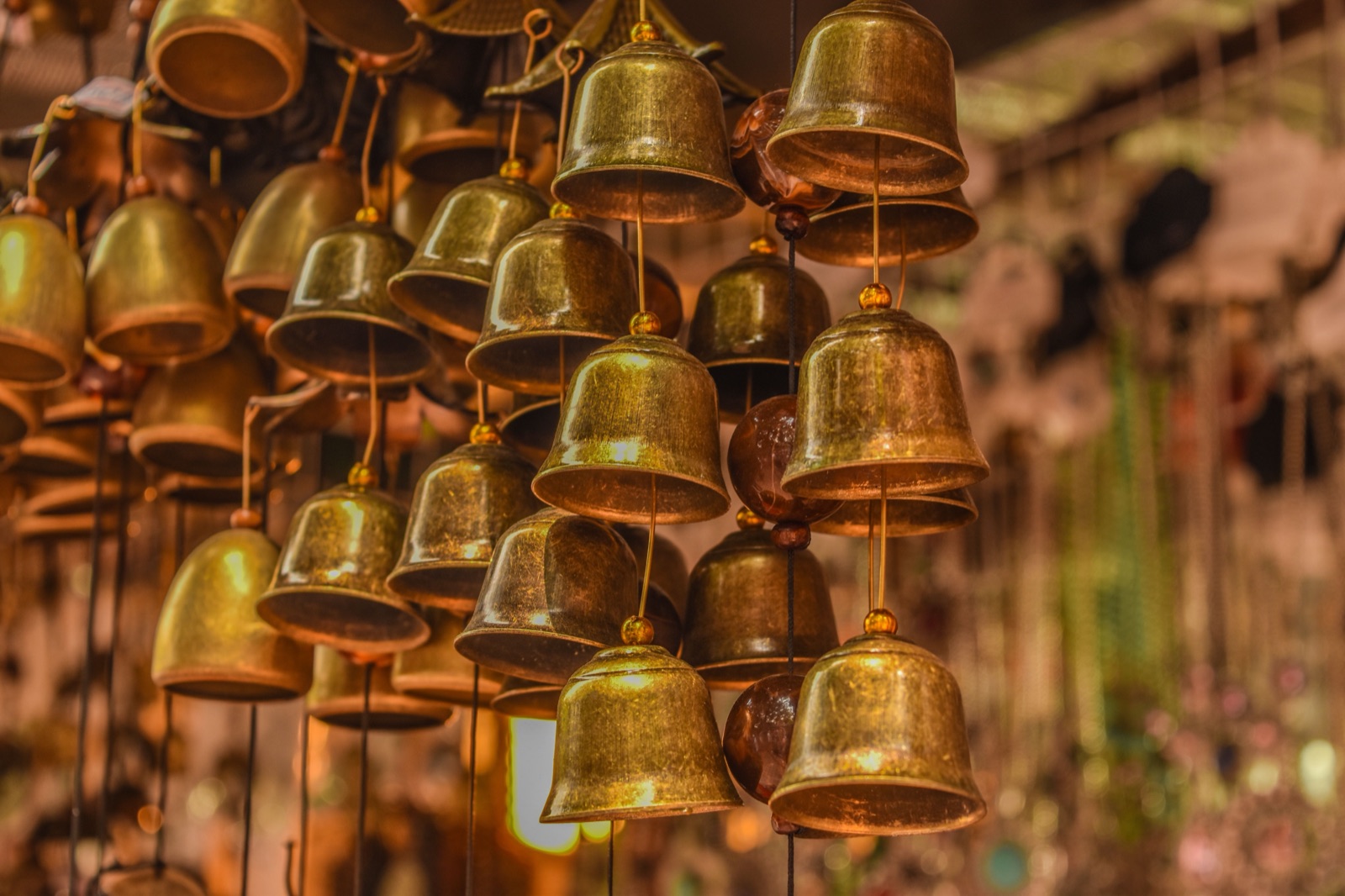 Close-up of small brass bells with a worn antique finish hanging on cords in clusters, with a soft blurred background.